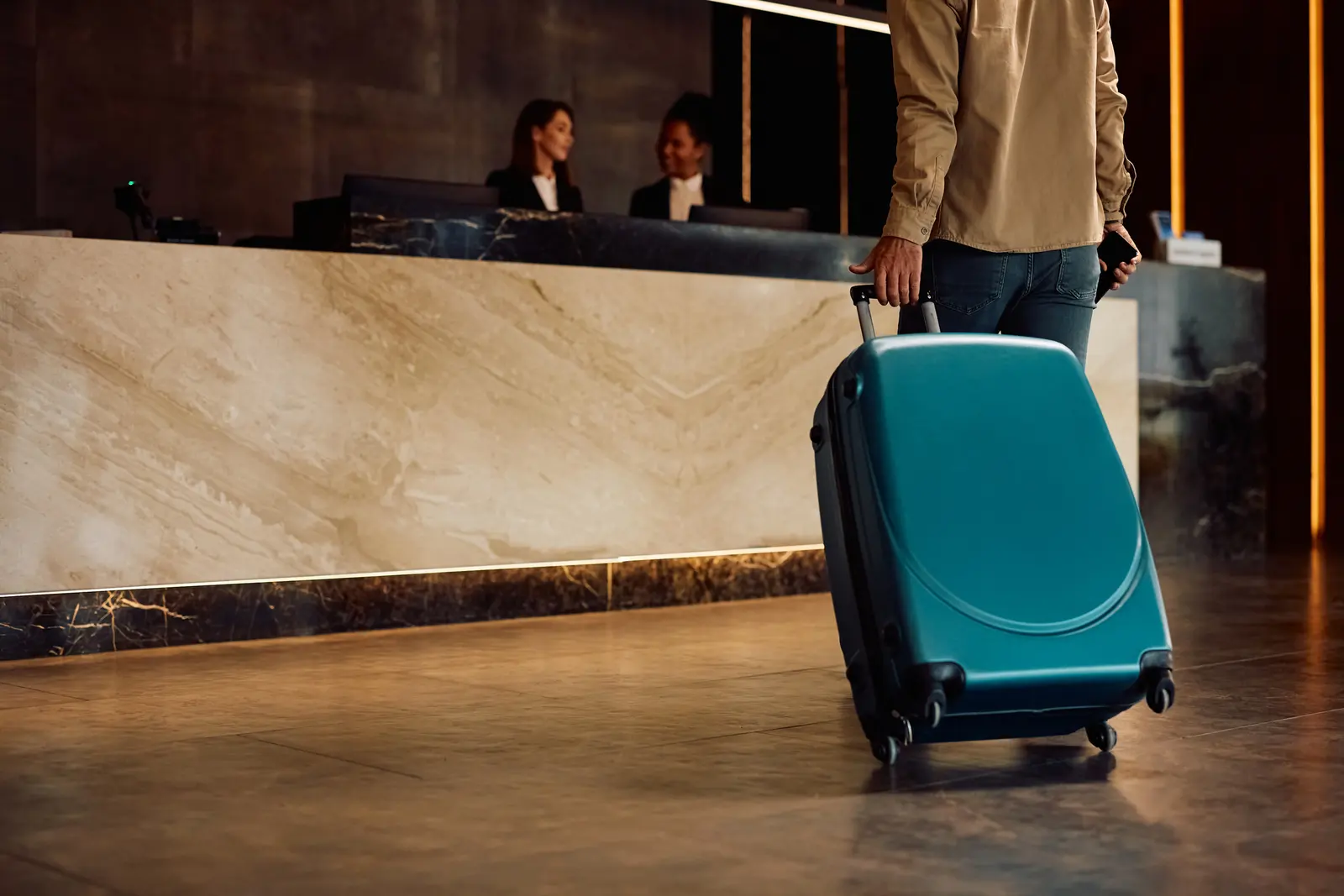 A guest with a suitcase at a marble hotel front desk