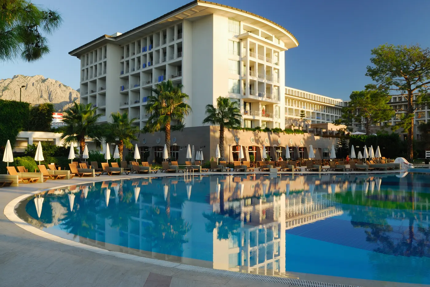 A resort hotel above its pool and sun loungers at golden hour, mountains behind